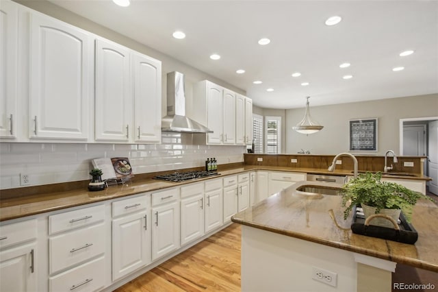 kitchen featuring stainless steel gas cooktop, tasteful backsplash, a sink, a peninsula, and wall chimney exhaust hood