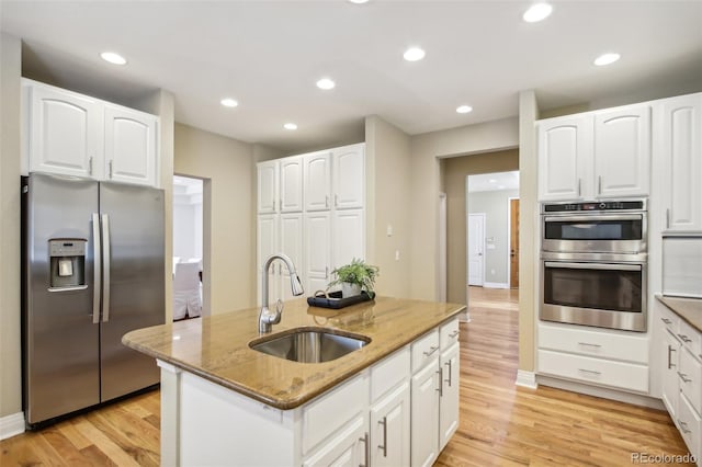 kitchen featuring light stone counters, stainless steel appliances, light wood-style flooring, a kitchen island with sink, and a sink