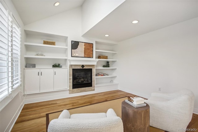 living room with built in shelves, a tile fireplace, recessed lighting, wood finished floors, and vaulted ceiling