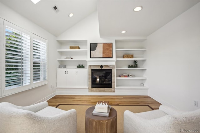 living room featuring built in features, a tile fireplace, visible vents, and wood finished floors