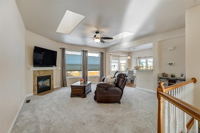 carpeted living room featuring a fireplace, ceiling fan, and a skylight