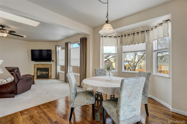 dining room featuring ceiling fan, a tile fireplace, hardwood / wood-style flooring, and plenty of natural light