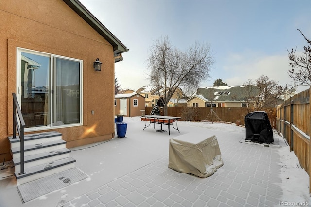 snow covered patio featuring a storage shed and area for grilling