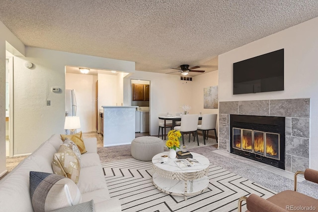 living area featuring a textured ceiling, carpet floors, a fireplace, washer / dryer, and ceiling fan