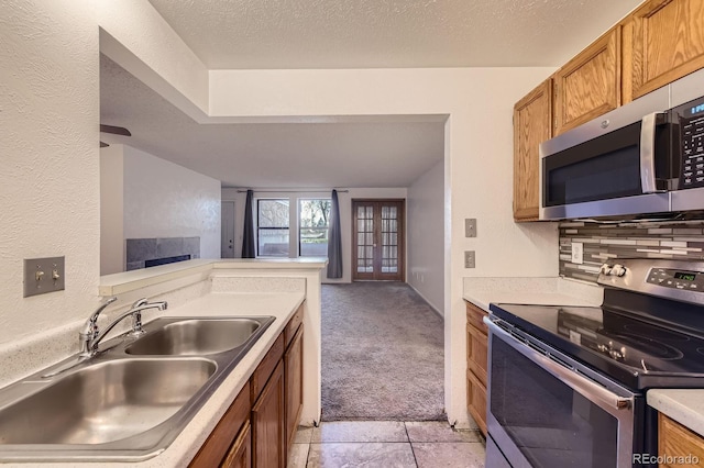 kitchen with light carpet, a sink, open floor plan, stainless steel appliances, and brown cabinetry