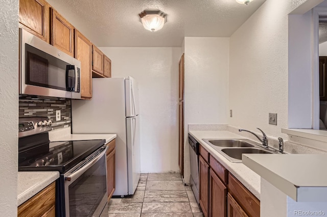 kitchen with brown cabinetry, a sink, stainless steel appliances, light countertops, and tasteful backsplash