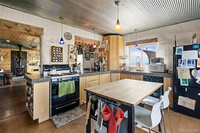 kitchen with black appliances, hanging light fixtures, light brown cabinets, and a wood stove