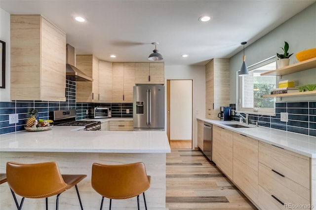 3010 Zinnia Ct, Golden, CO 80401 - kitchen featuring appliances with stainless steel finishes, wall chimney exhaust hood, light brown cabinetry, a peninsula, and a sink