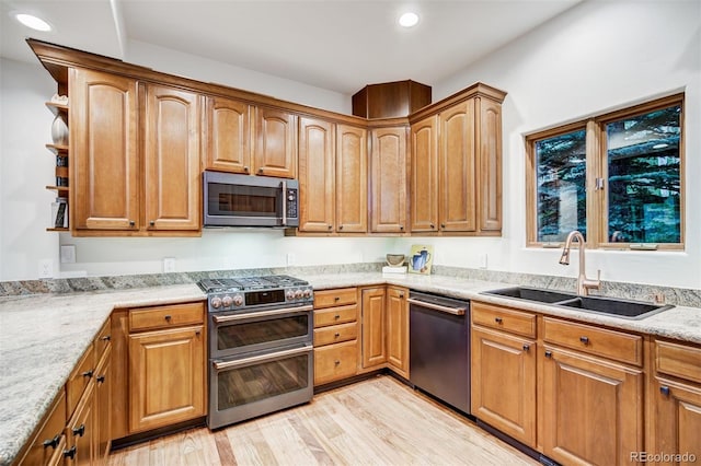 kitchen with appliances with stainless steel finishes, sink, light stone counters, and light hardwood / wood-style floors