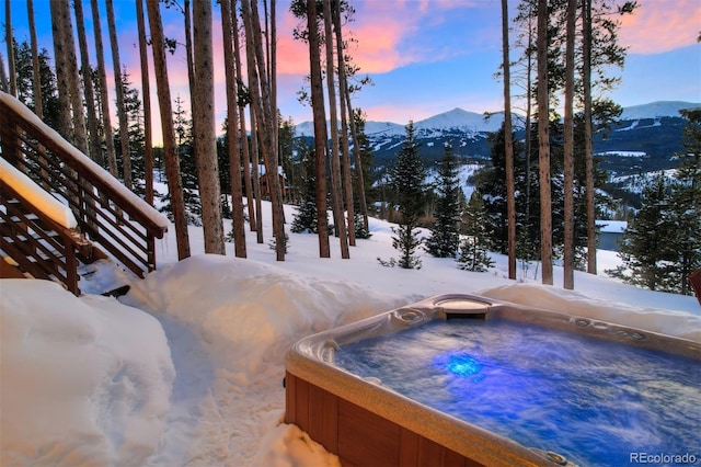 yard covered in snow with a mountain view and a hot tub