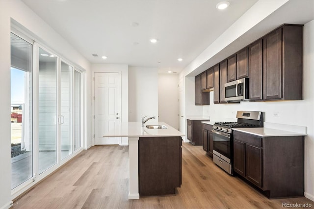 kitchen featuring sink, appliances with stainless steel finishes, dark brown cabinetry, an island with sink, and light wood-type flooring