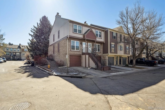 view of property with brick siding, a chimney, an attached garage, a residential view, and stairs