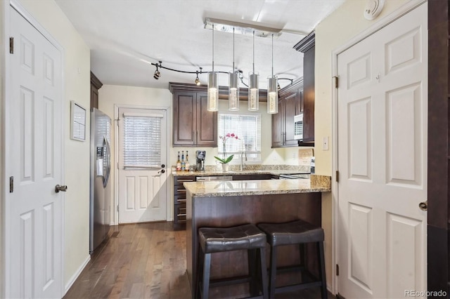 kitchen featuring dark brown cabinetry, a peninsula, dark wood-type flooring, stainless steel fridge with ice dispenser, and light stone countertops