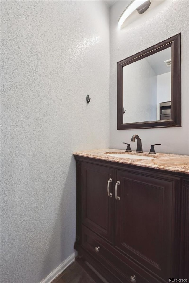 bathroom with a textured wall, baseboards, visible vents, and vanity