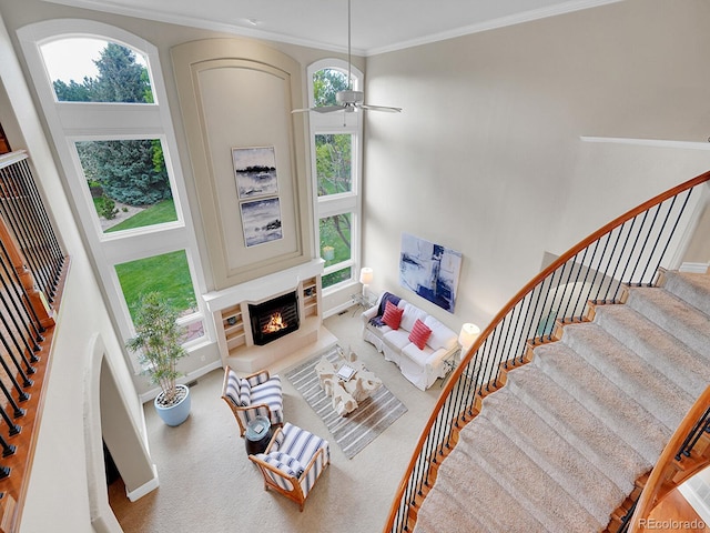 291 Fairchild Dr, Highlands Ranch, CO 80126 - living area with a lit fireplace, stairs, a towering ceiling, crown molding, and ceiling fan
