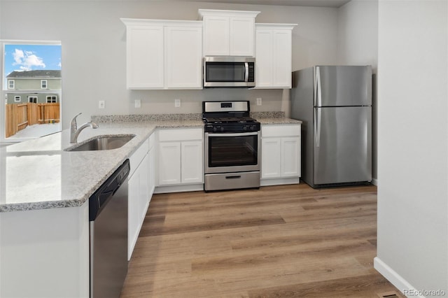 kitchen featuring stainless steel appliances, a sink, white cabinets, a peninsula, and light stone countertops