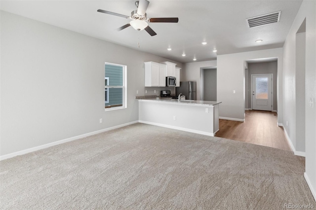 kitchen with stainless steel appliances, white cabinetry, light colored carpet, baseboards, and ceiling fan