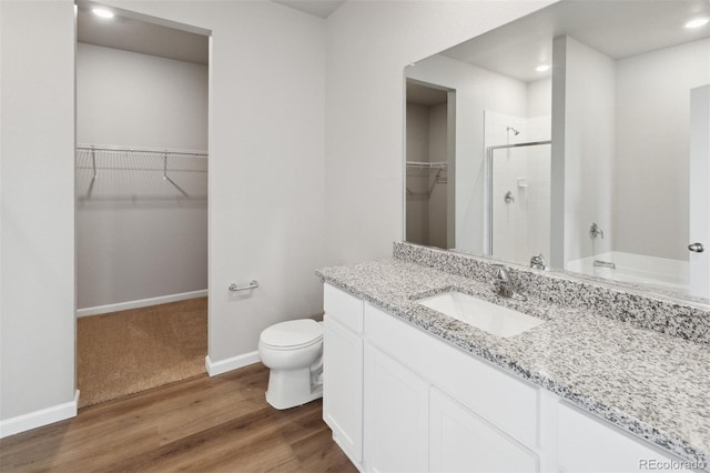 bathroom with a shower stall, wood finished floors, toilet, baseboards, and a walk in closet