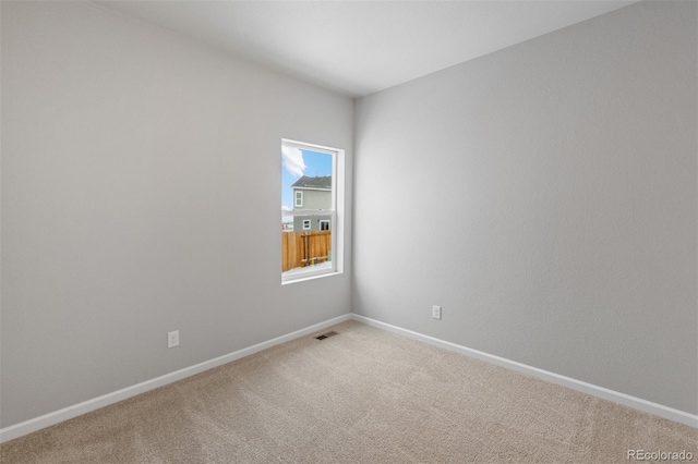 spare room featuring light carpet and baseboards