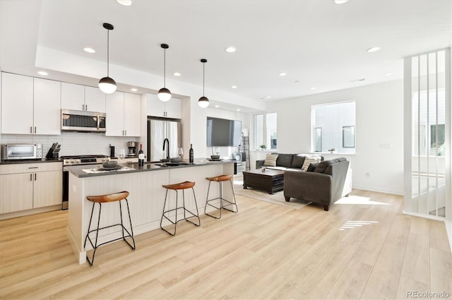 kitchen with a kitchen bar, appliances with stainless steel finishes, light wood-type flooring, white cabinets, and hanging light fixtures