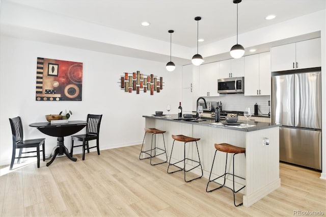 kitchen featuring appliances with stainless steel finishes, backsplash, white cabinets, hanging light fixtures, and a breakfast bar area