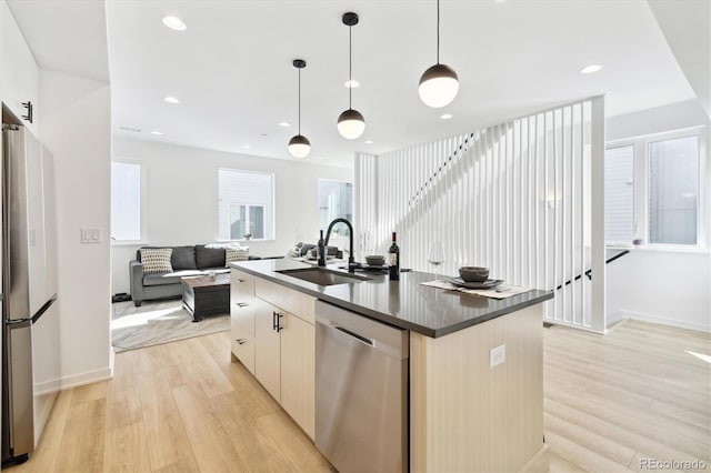 kitchen featuring appliances with stainless steel finishes, a kitchen island with sink, sink, light hardwood / wood-style flooring, and hanging light fixtures