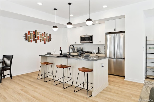 kitchen with decorative light fixtures, white cabinetry, stainless steel appliances, and a breakfast bar area