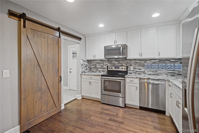 kitchen featuring appliances with stainless steel finishes, dark hardwood / wood-style floors, light stone counters, white cabinets, and a barn door