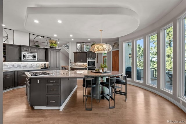 kitchen featuring a breakfast bar, pendant lighting, a kitchen island with sink, stainless steel appliances, and dark brown cabinets