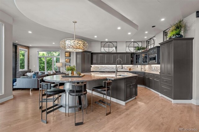 kitchen with pendant lighting, light hardwood / wood-style flooring, a kitchen island with sink, light stone countertops, and a kitchen bar