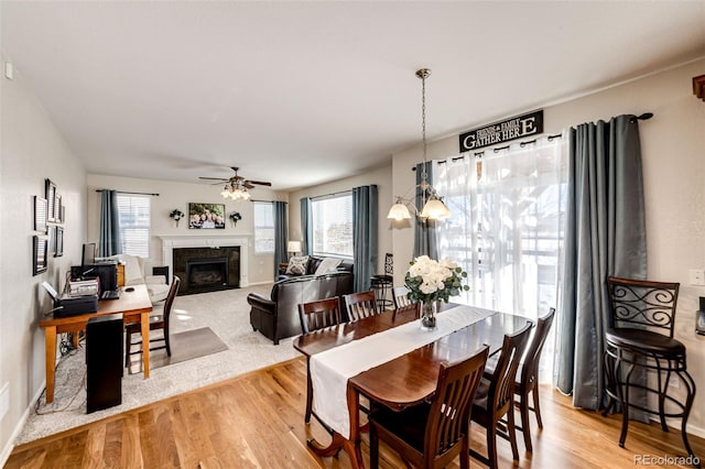 dining space with a high end fireplace, ceiling fan with notable chandelier, and light hardwood / wood-style flooring