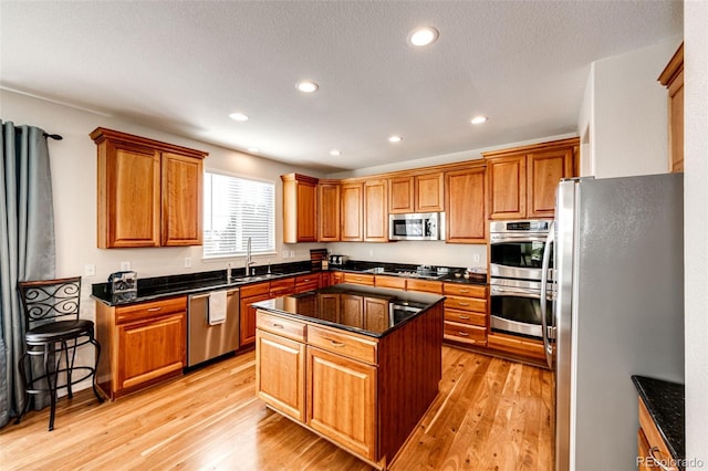 kitchen with light hardwood / wood-style floors, appliances with stainless steel finishes, a center island, dark stone counters, and sink