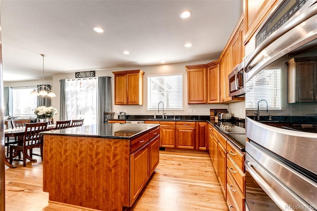 kitchen with a healthy amount of sunlight, a notable chandelier, dark stone counters, a kitchen island, and sink