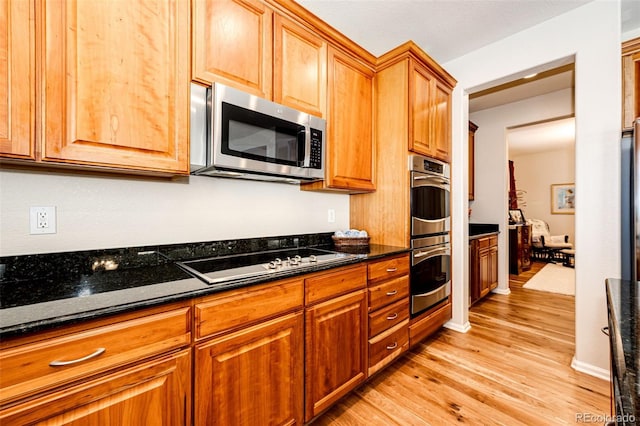 kitchen with appliances with stainless steel finishes, dark stone counters, and light wood-type flooring