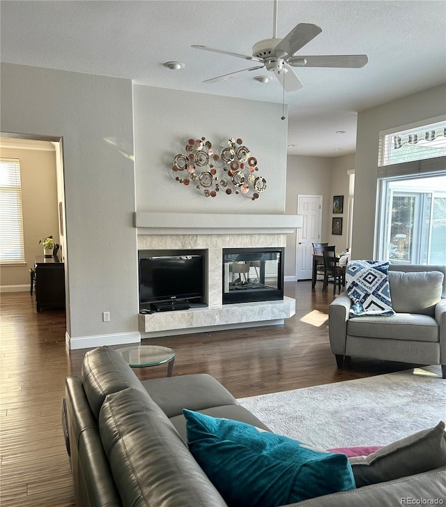 living room with dark wood-type flooring, ceiling fan, a high end fireplace, and a textured ceiling