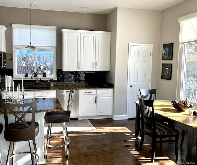 kitchen with white cabinetry, backsplash, decorative light fixtures, stainless steel dishwasher, and dark stone counters