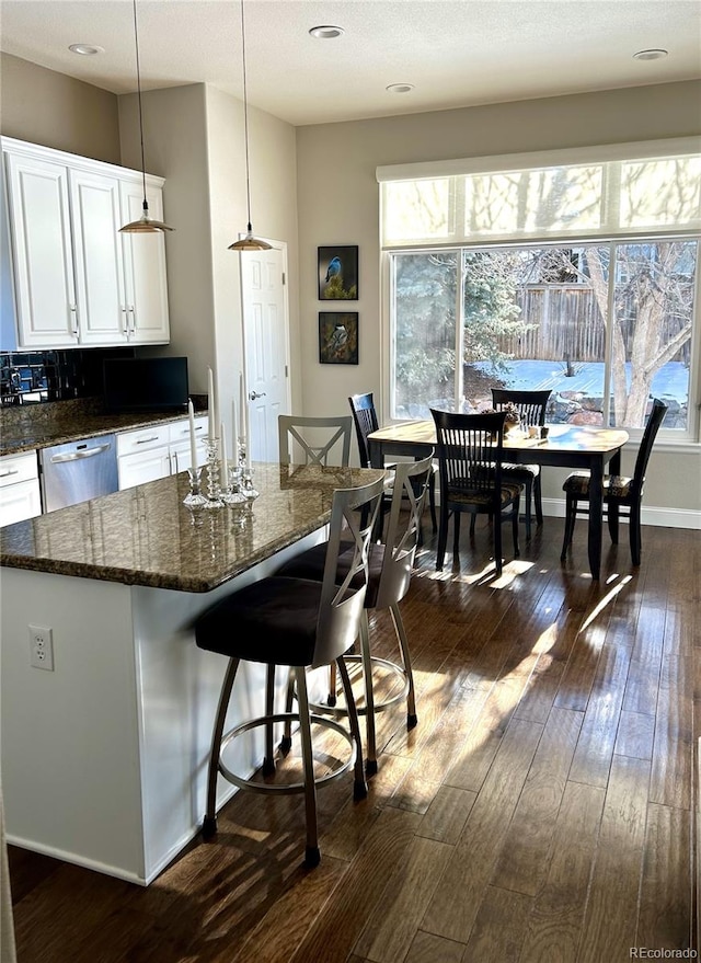 kitchen with dishwasher, white cabinetry, a kitchen breakfast bar, a wealth of natural light, and decorative light fixtures