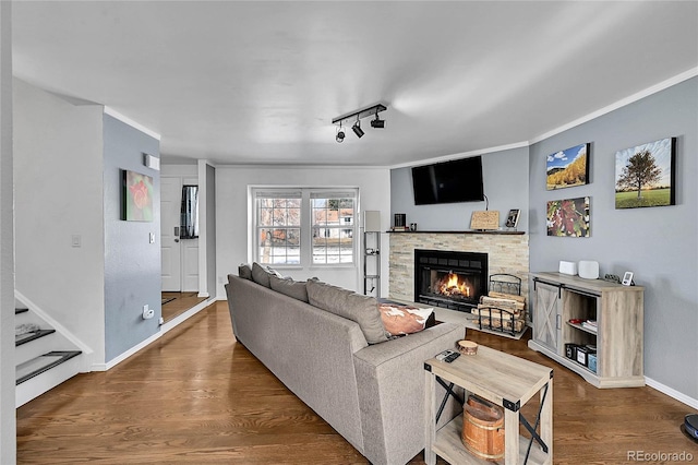 living room featuring ornamental molding, a stone fireplace, baseboards, and wood finished floors