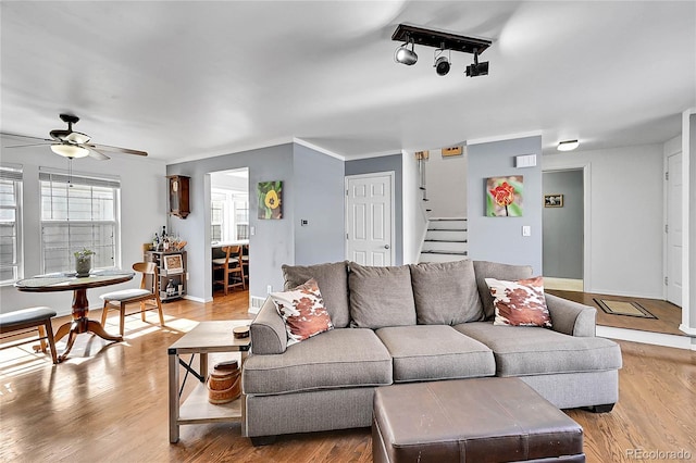 living area with light wood-style flooring, ceiling fan, stairway, and baseboards