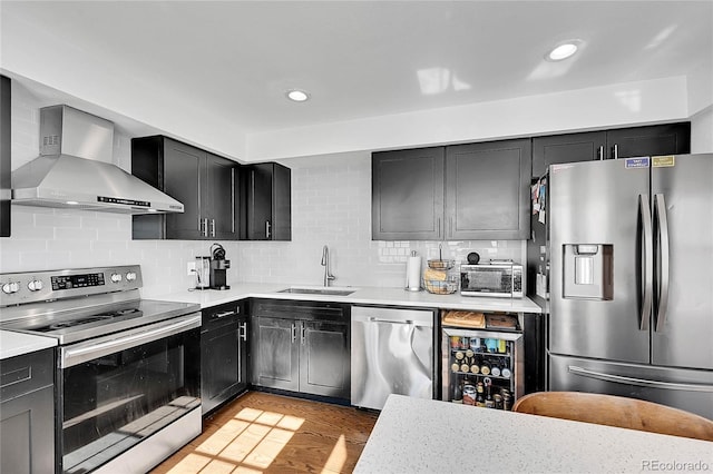 kitchen featuring wall chimney range hood, a sink, appliances with stainless steel finishes, and dark cabinetry