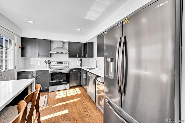 kitchen featuring a sink, light wood-style floors, appliances with stainless steel finishes, wall chimney exhaust hood, and tasteful backsplash