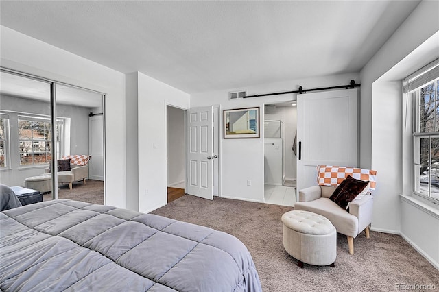 bedroom with a barn door, visible vents, baseboards, carpet, and a closet