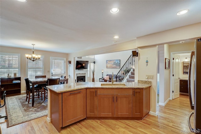 8754 Mesquite Row, Lone Tree, CO 80124 - kitchen with a fireplace, brown cabinetry, light wood-type flooring, light stone counters, and open floor plan