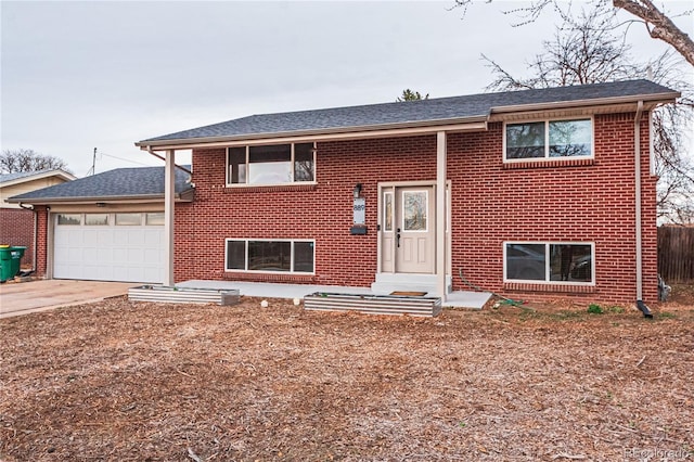 bi-level home featuring a garage, fence, concrete driveway, brick siding, and roof with shingles