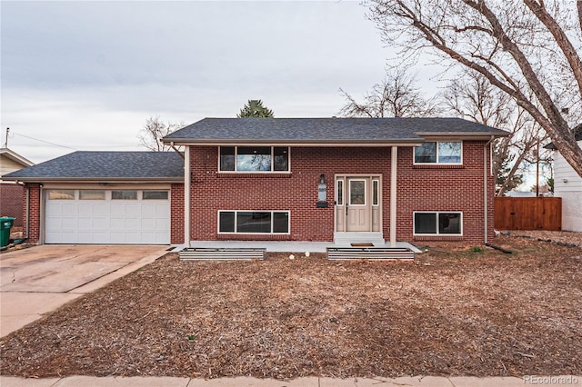split foyer home with roof with shingles, fence, brick siding, an attached garage, and driveway