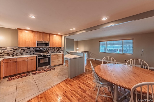 kitchen featuring light wood-style floors, tasteful backsplash, stainless steel microwave, light countertops, and electric range oven
