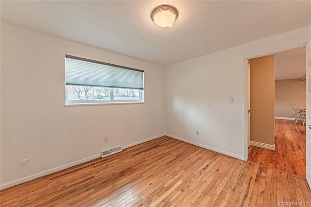 spare room featuring light wood finished floors, visible vents, and baseboards