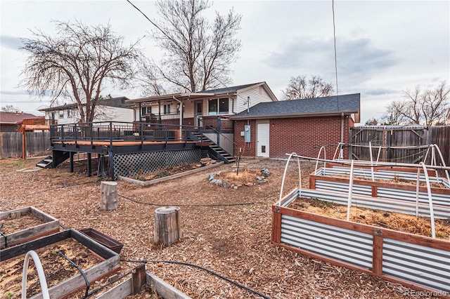 rear view of house with brick siding, a garden, a fenced backyard, and a wooden deck