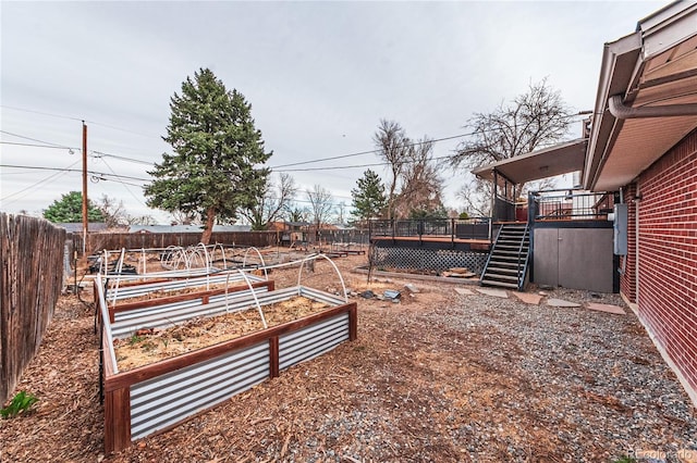 view of yard with stairs, a fenced backyard, a wooden deck, and a vegetable garden