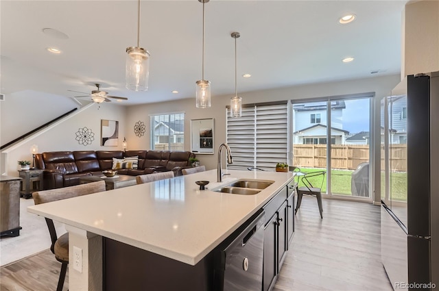 kitchen featuring sink, dishwasher, ceiling fan, hanging light fixtures, and a center island with sink